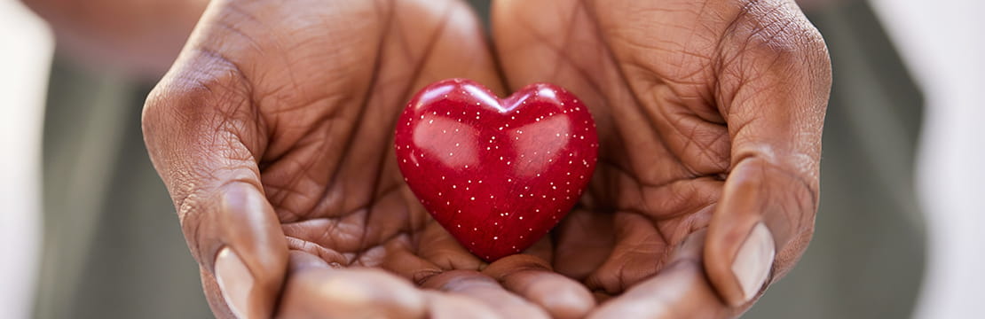 Close up of black woman hands holding a small red heart.