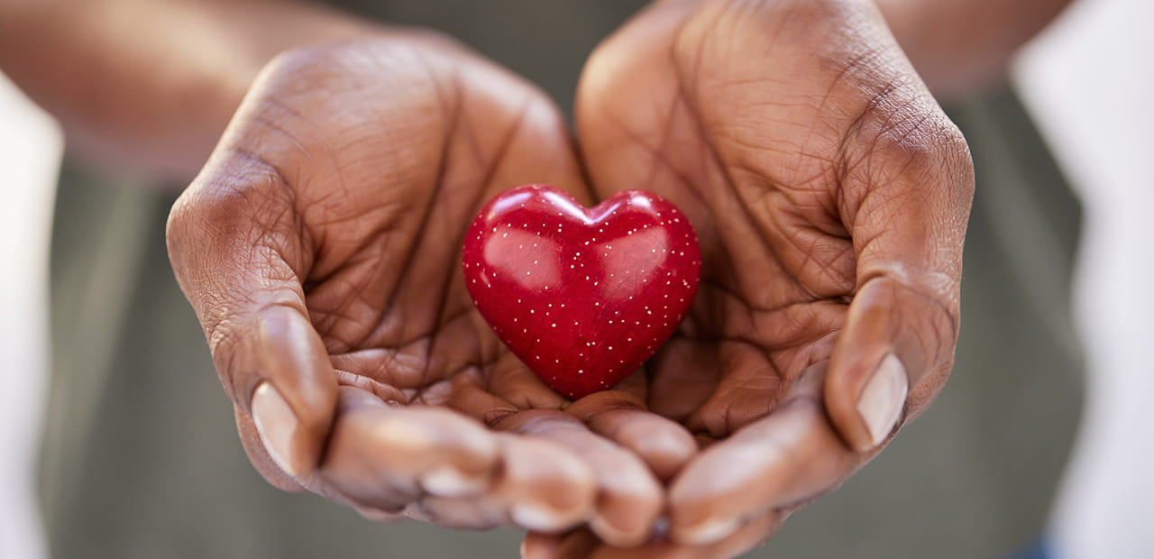 Close up of black woman hands holding a small red heart.