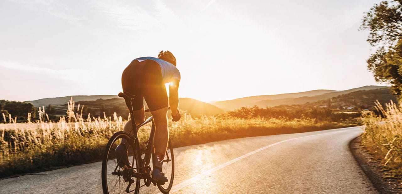 Cyclist rides on a rural road at sunset.