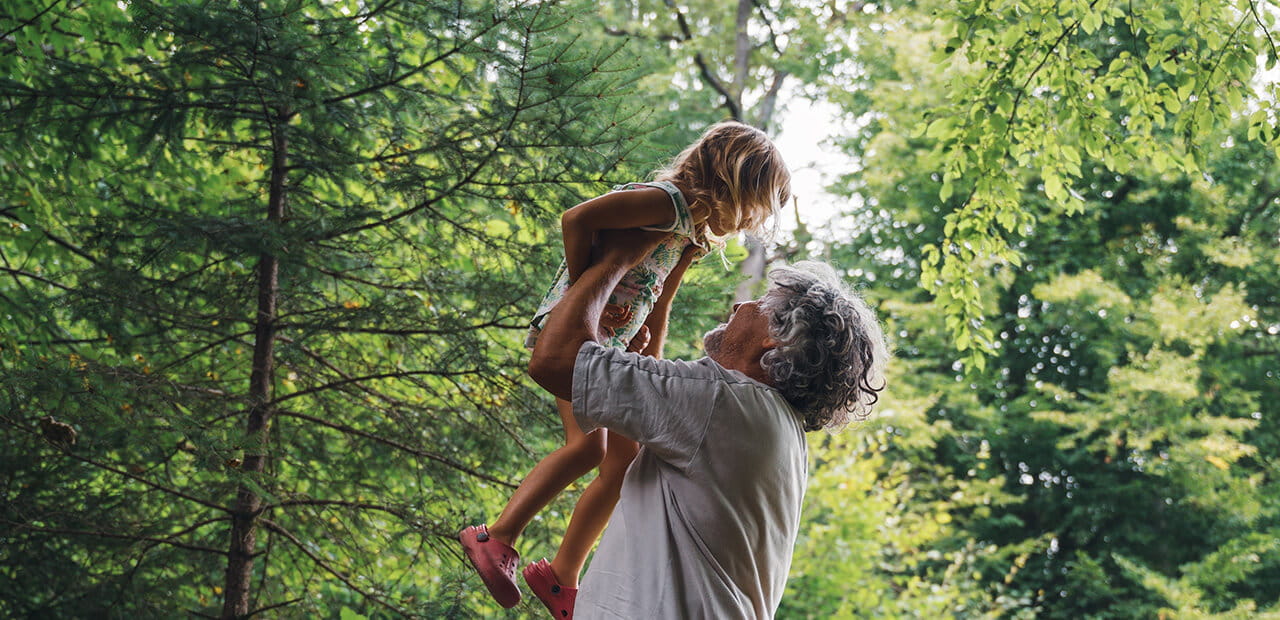  grandpa lifting grandchild high up in the air outside in green summer forest.