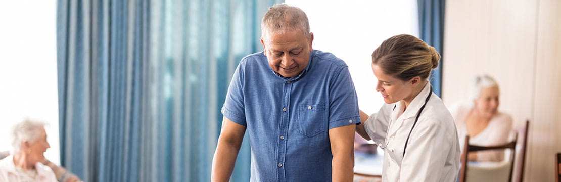 Female doctor assisting senior man walking with walker at retirement home.