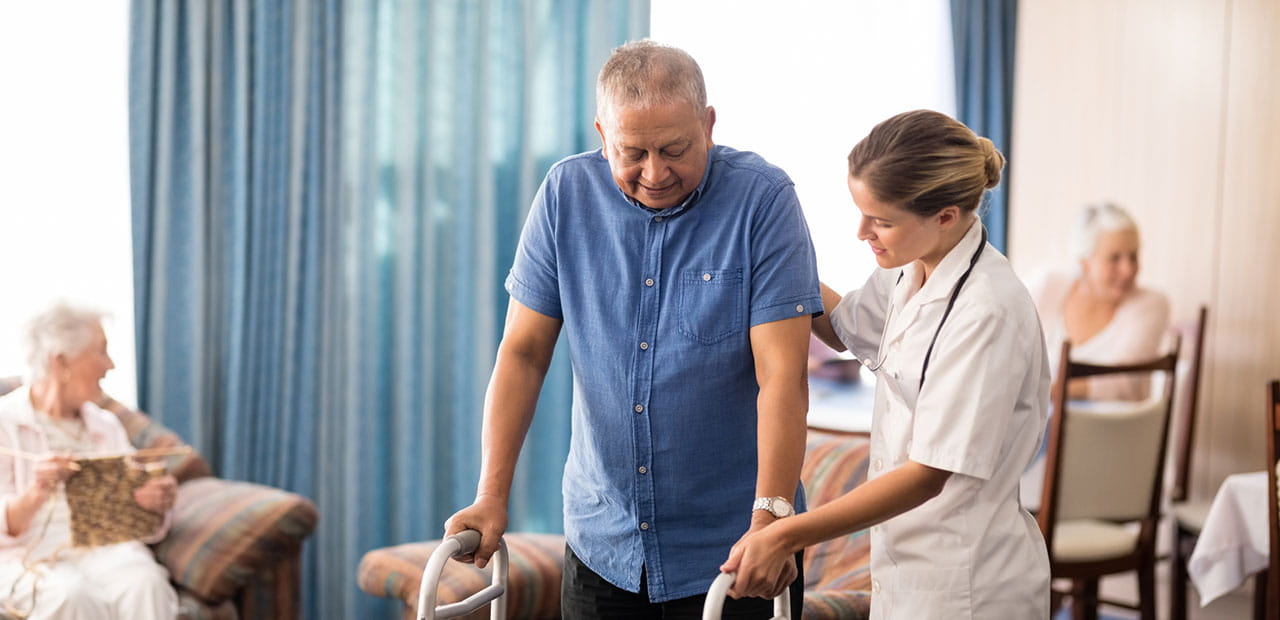 Female doctor assisting senior man walking with walker at retirement home.