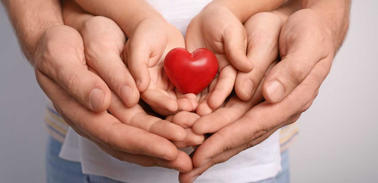 Close up of a family holding small red heart in their hands.
