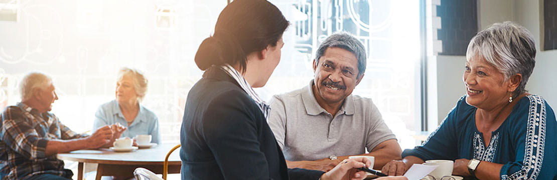 An elderly couple having a conversation with a professional. Another elderly couple sitting in the background.