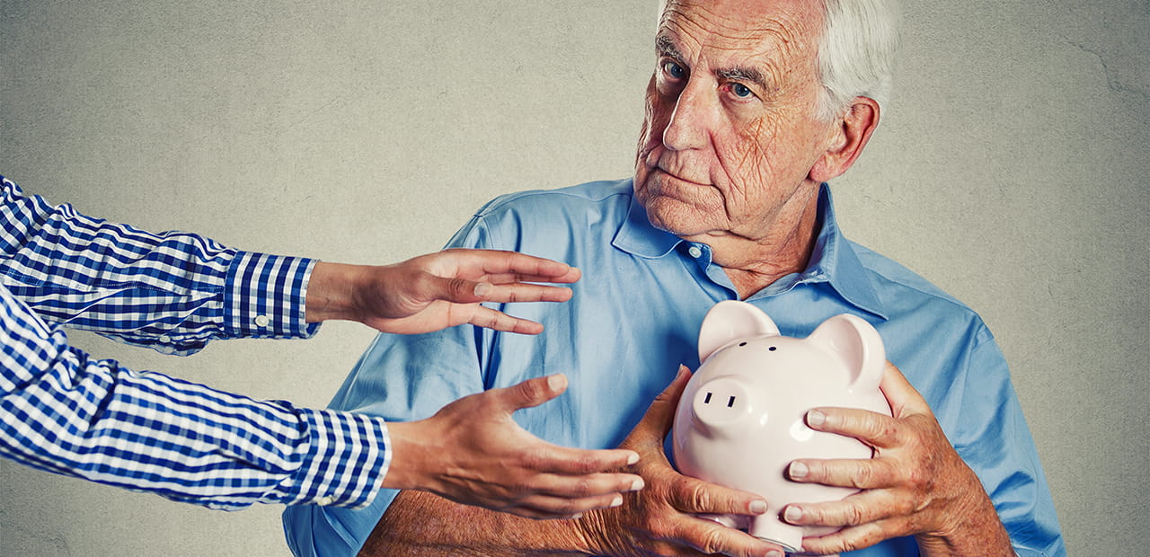 Close up portrait of elderly man holding piggy bank, looking suspicious trying to protect his savings from being stolen from outstretched arms. Financial fraud concept
