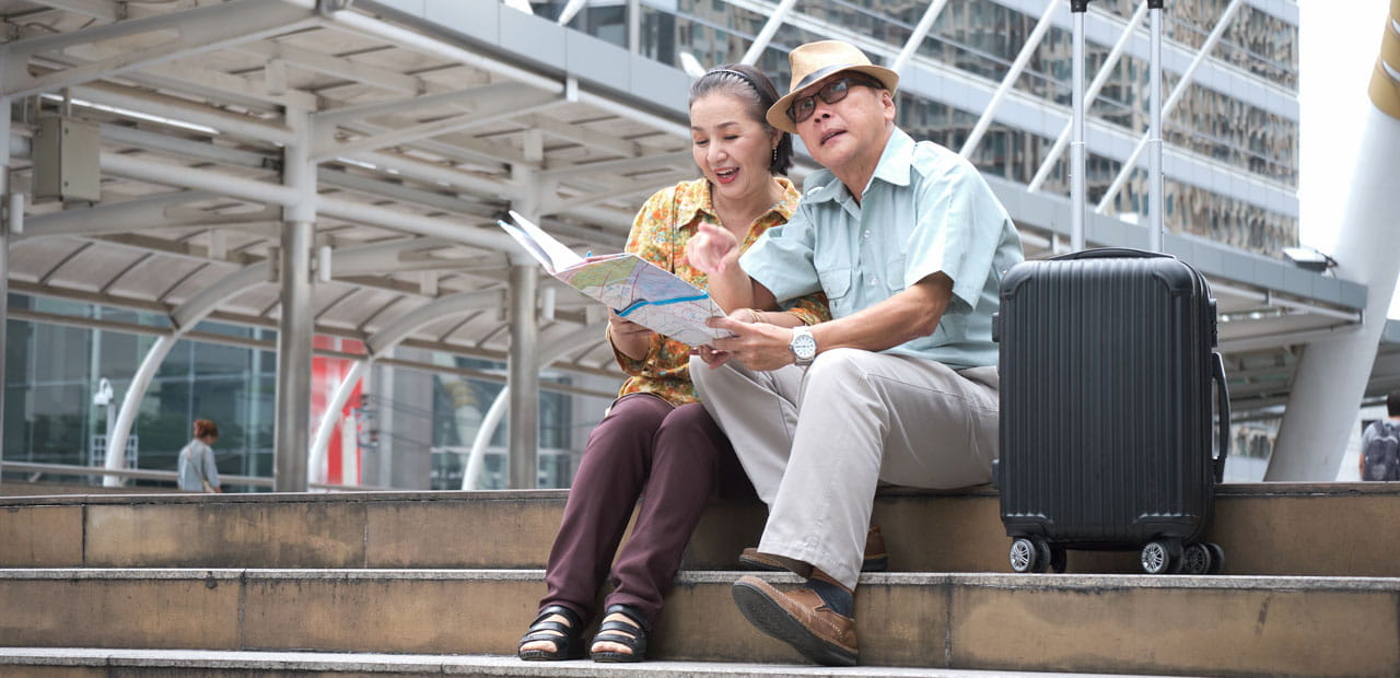 A senior Asian couple sitting on the stairs, holding a map.
