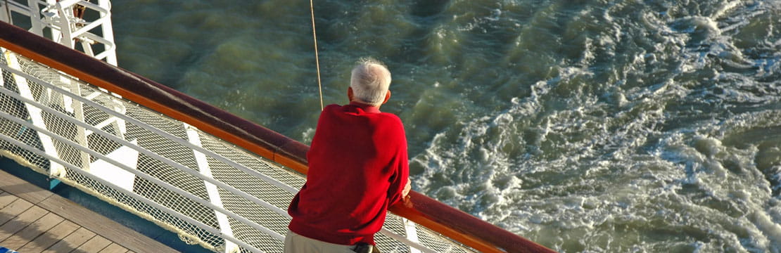 A senior man looks out over the rail of a cruise ship.
