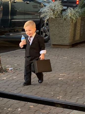 little boy dressed up in suit with brief case and bottle